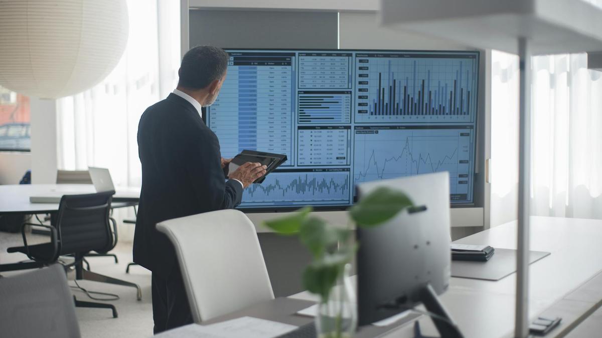 Professional in suit analyzing financial data on screens in a modern office setting.