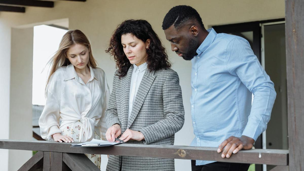 Three adults reviewing documents on a balcony during a real estate consultation.