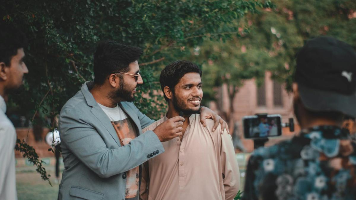 Two men casually interacting outdoors with a live recording setup, surrounded by greenery.