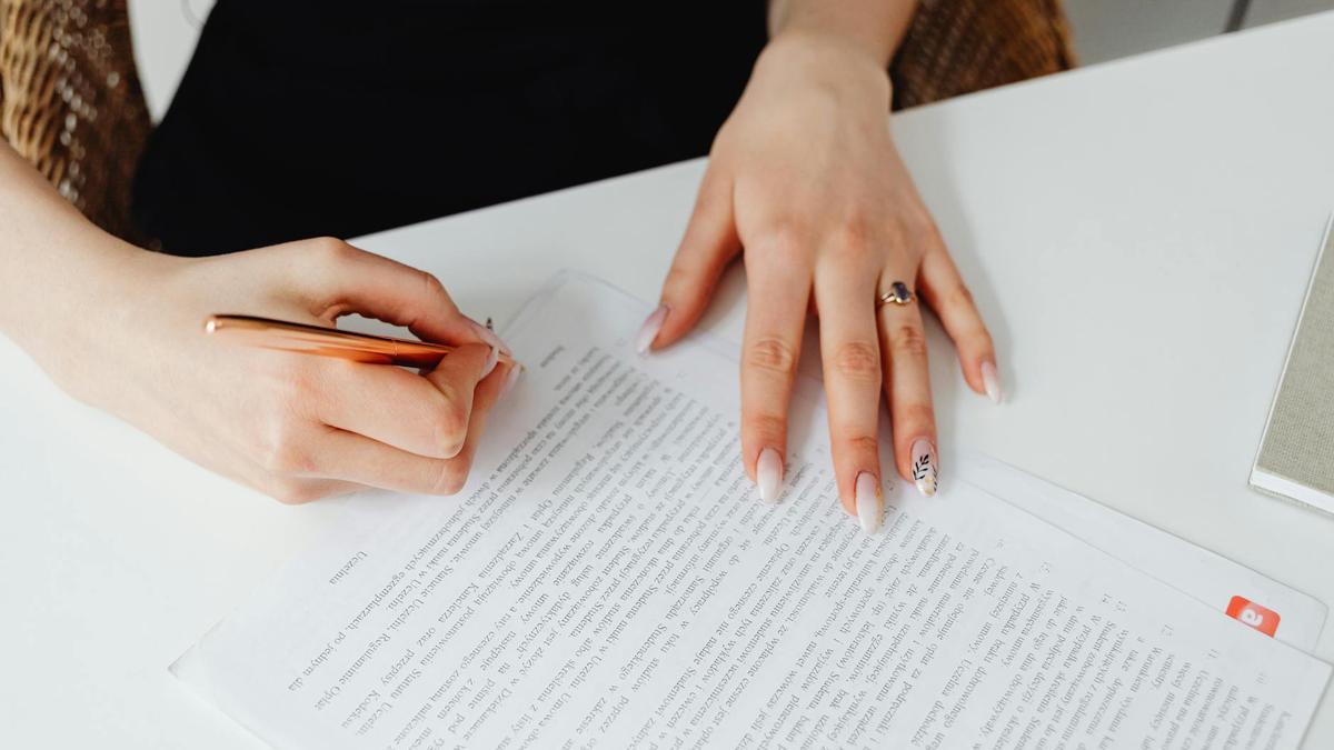 A woman signing a document with a pen on a desk, emphasizing hands and writing.