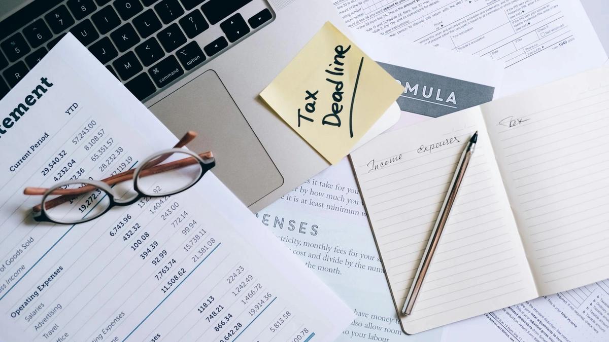 Workspace with laptop, documents, and tax deadline note for financial management.