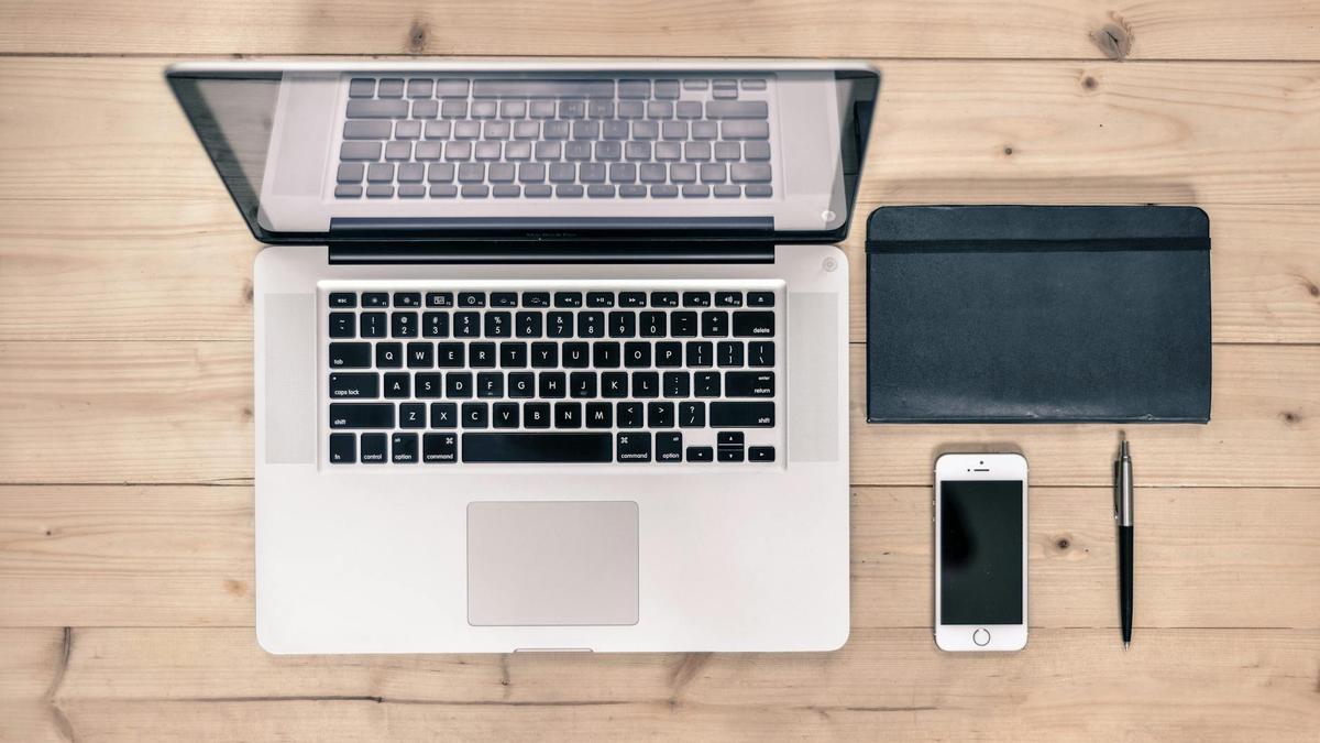 Top view of a tidy workspace featuring a laptop, smartphone, notebook, and pen on a wooden desk.