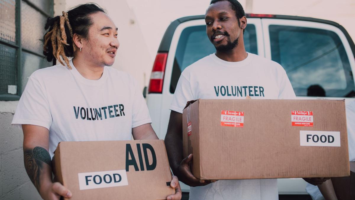 Two volunteers distributing food aid boxes for community relief outdoors.