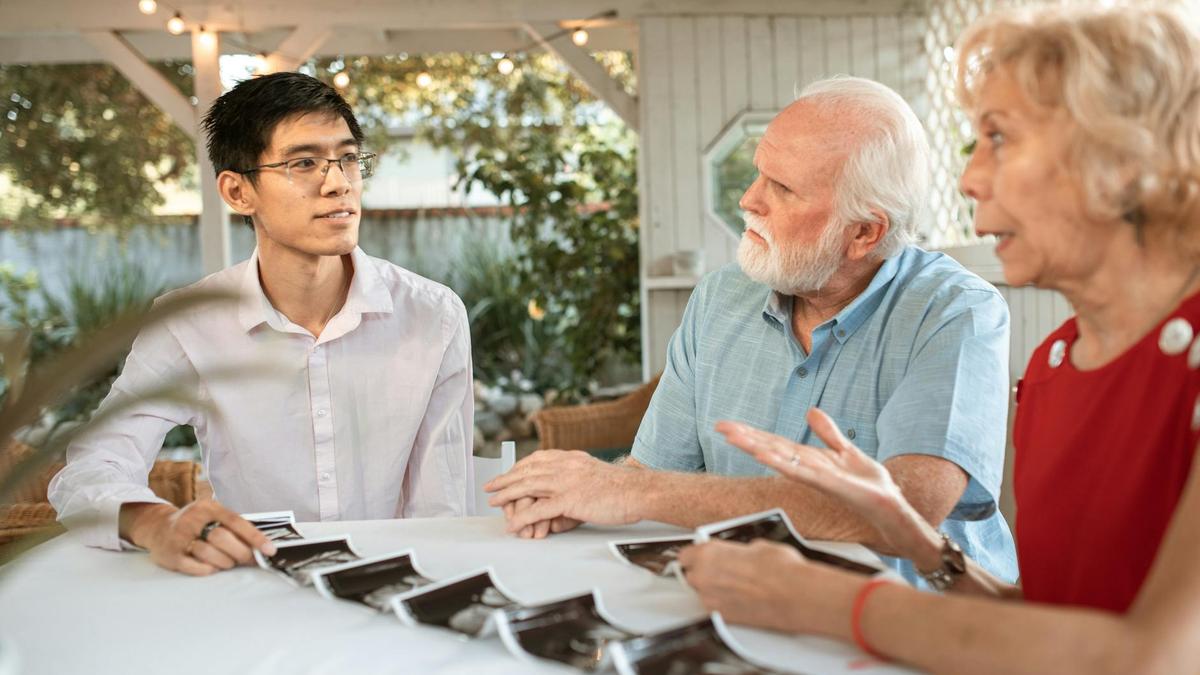 Senior couple and family member discussing ultrasound photos at an outdoor table.