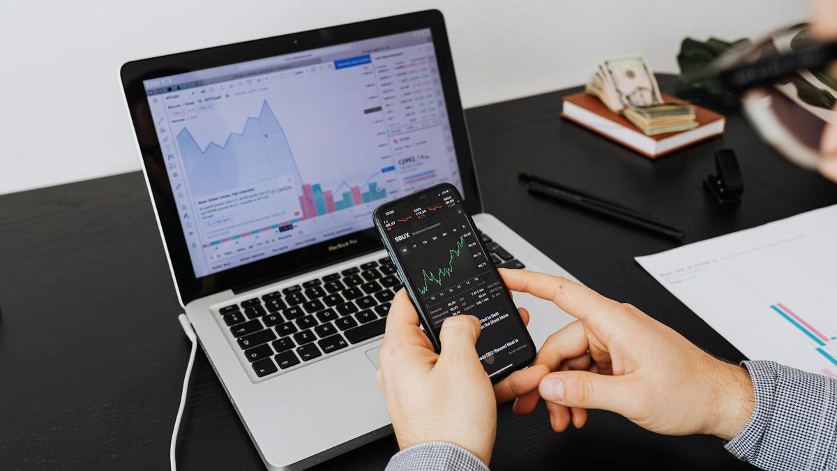 Person analyzing stock market data on a laptop and smartphone indoors.