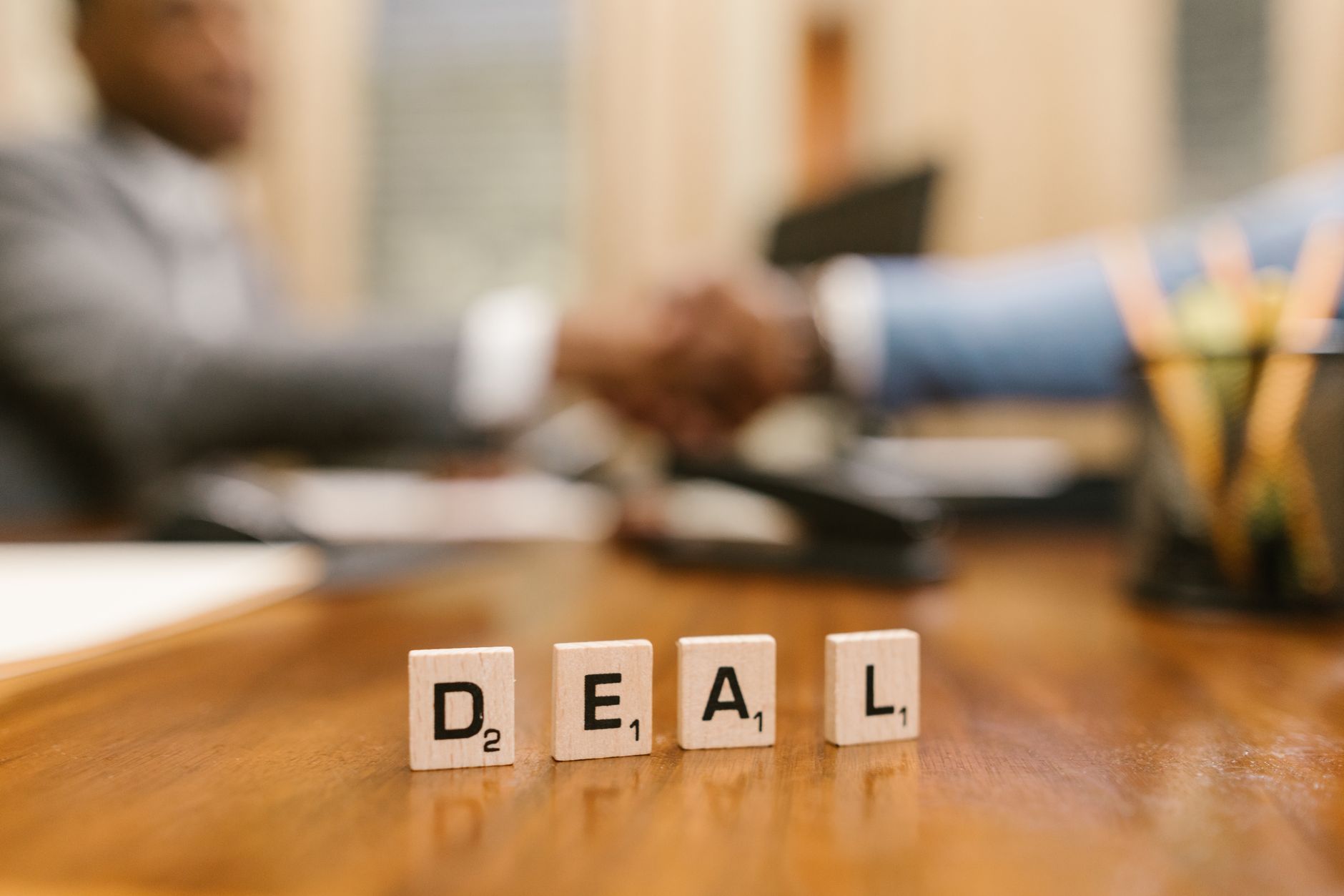 Close-up of Scrabble tiles spelling 'deal' with a handshake in the background.