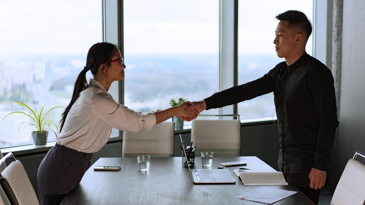 Professional coworkers exchange a handshake in a modern corporate office setting.