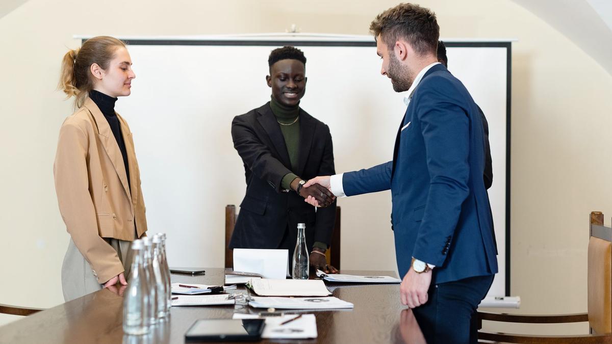 A diverse group of business professionals in a meeting room, shaking hands as a sign of agreement.