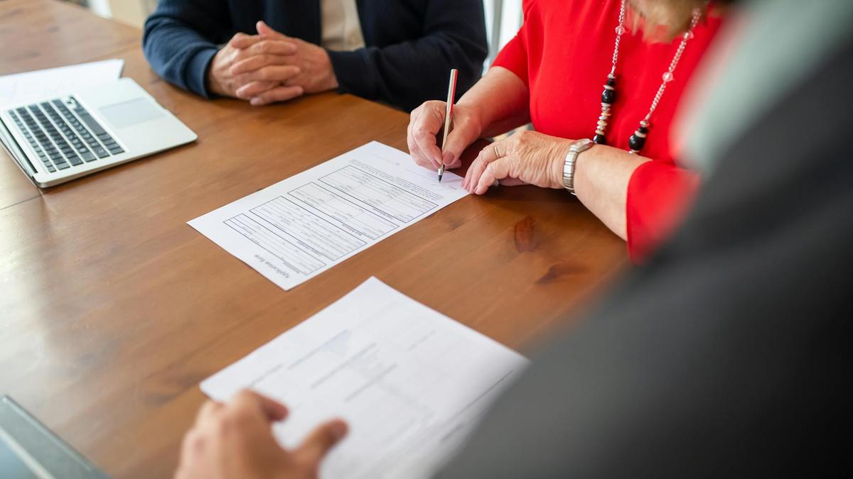 Two adults sign documents on a wooden table at a business meeting, emphasizing teamwork.