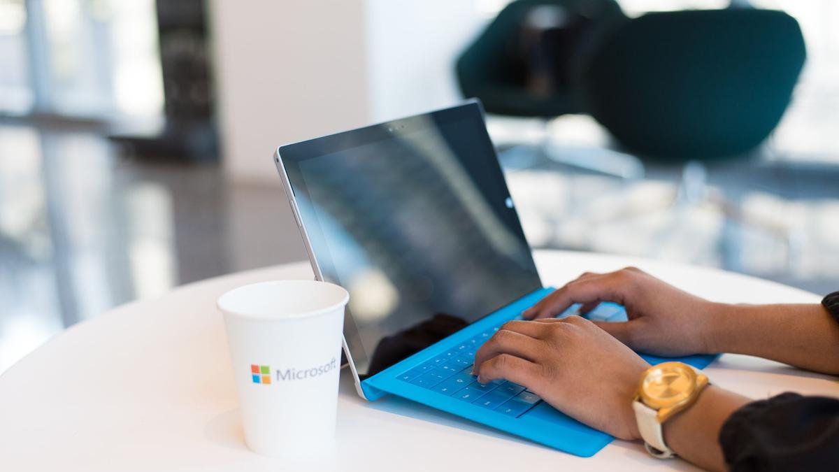 Hands typing on a blue keyboard with a branded cup on a table.