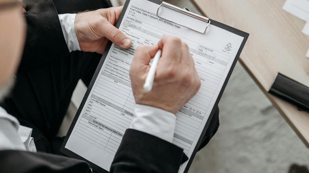 Close-up of a businessman signing a formal document on a clipboard.