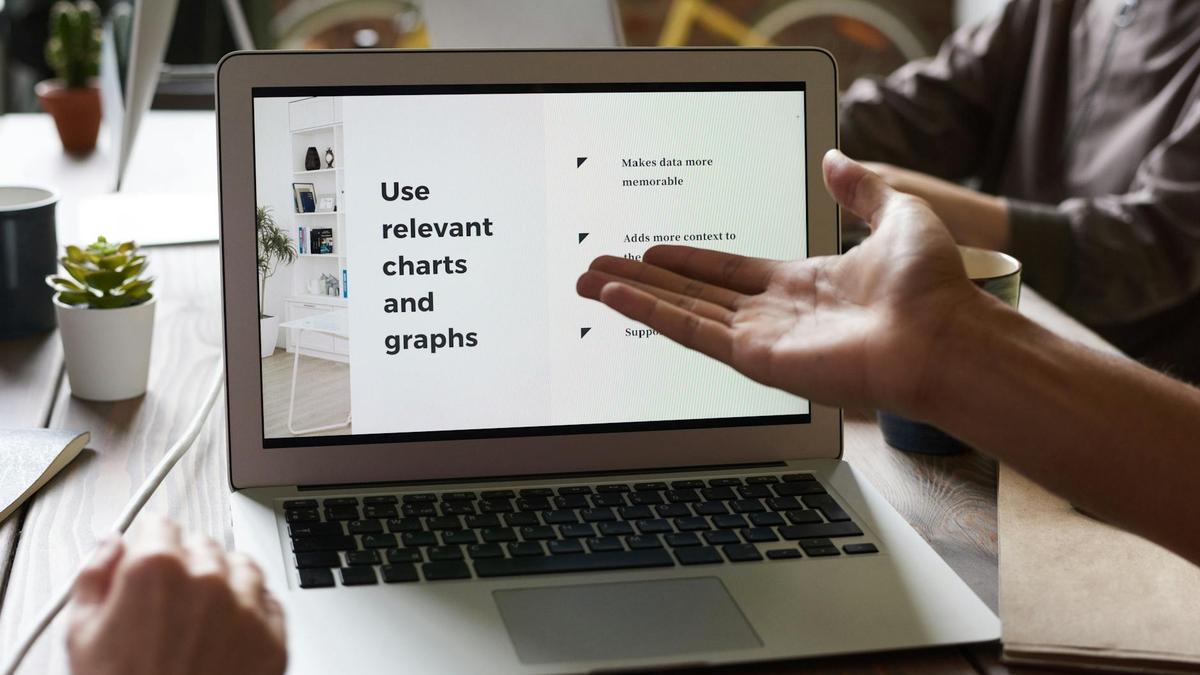 Close-up of a business meeting with hands gesturing toward a laptop screen.