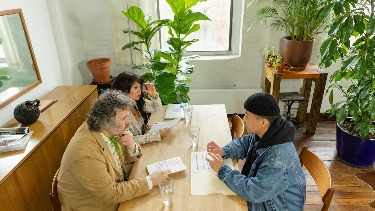 A casual business meeting with diverse colleagues around a wooden table in a plant-filled office.