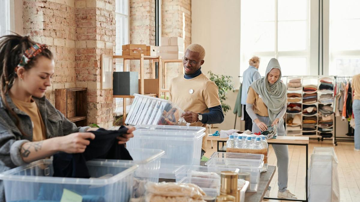 Group of diverse volunteers organizing donated clothing and supplies in a bright, airy warehouse.