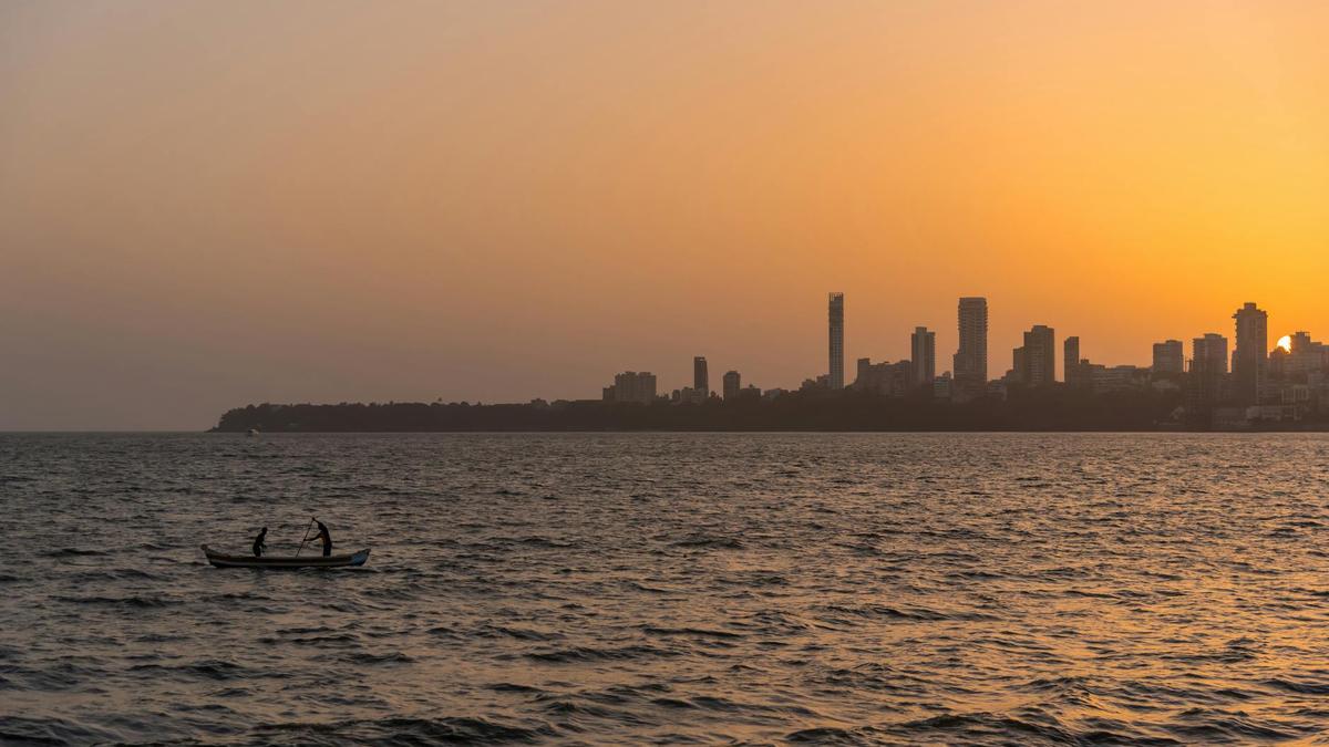 Silhouette of fishermen on a boat at sunset with a city skyline in the background.