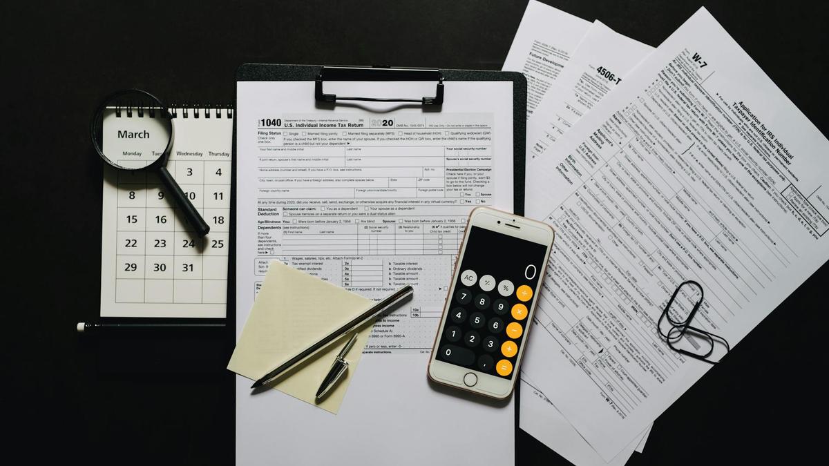 Top view of tax documents, calculator, magnifying glass, and calendar on a black surface.