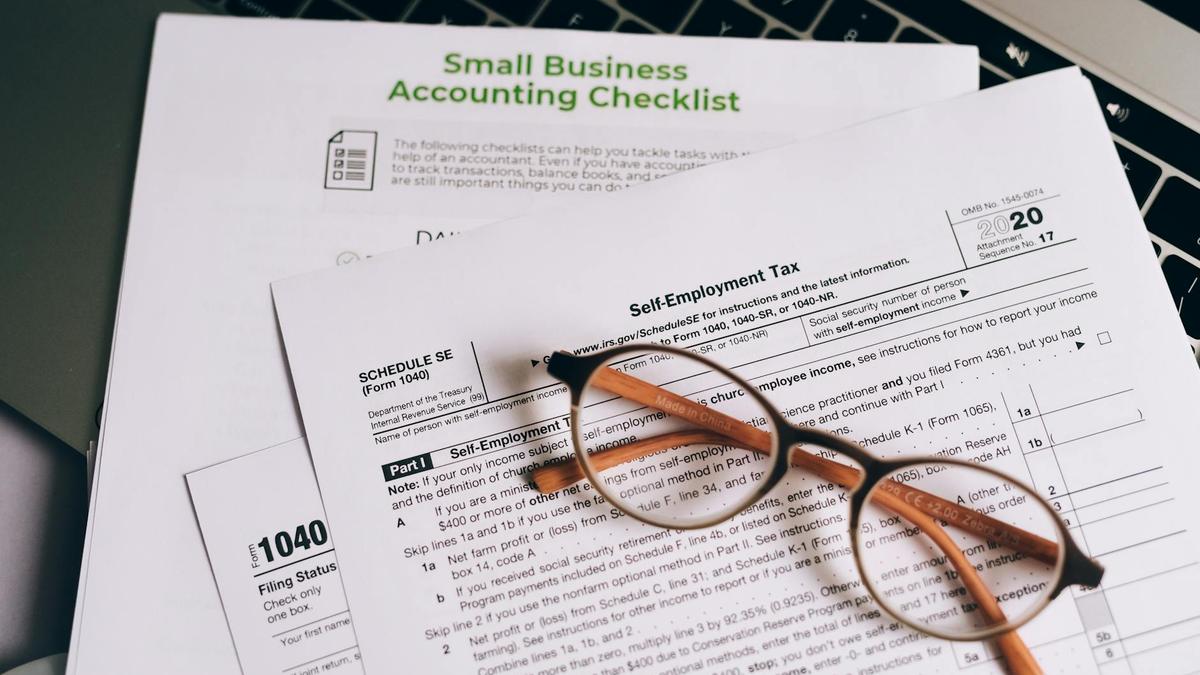 Close-up of tax forms and a small business accounting checklist on a laptop.