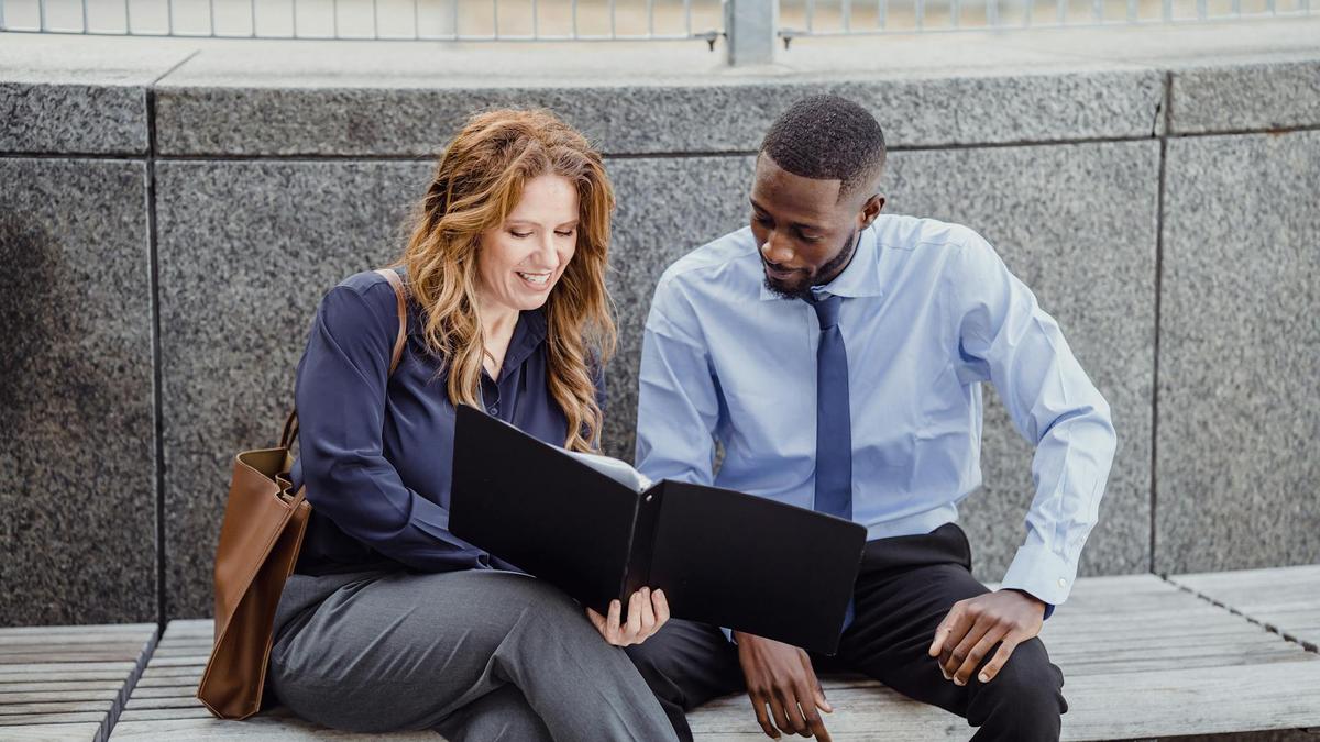 Two colleagues discussing a document while seated on an outdoor bench, showcasing teamwork.