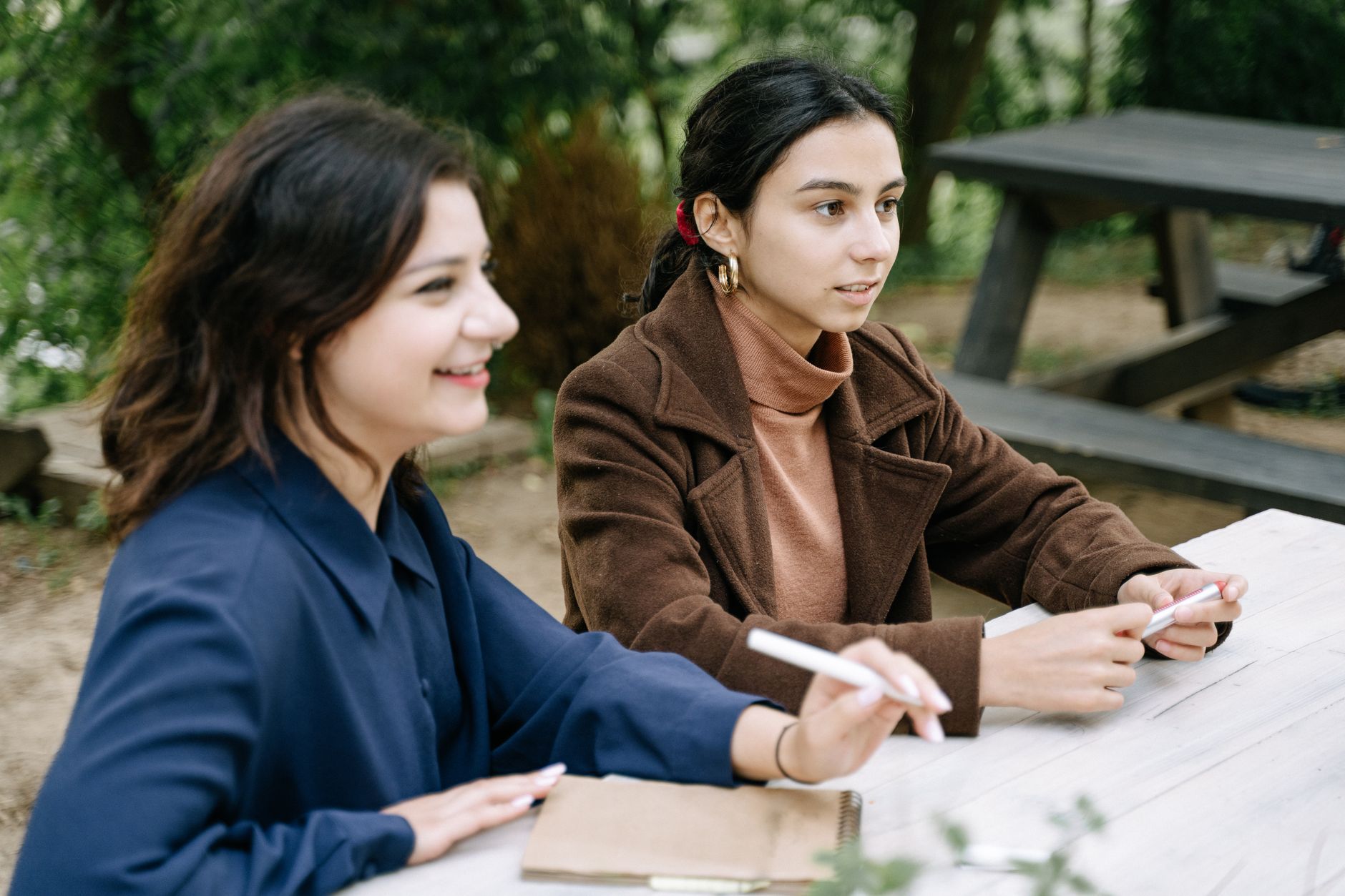 Two young women engaged in a collaborative discussion at an outdoor picnic table.