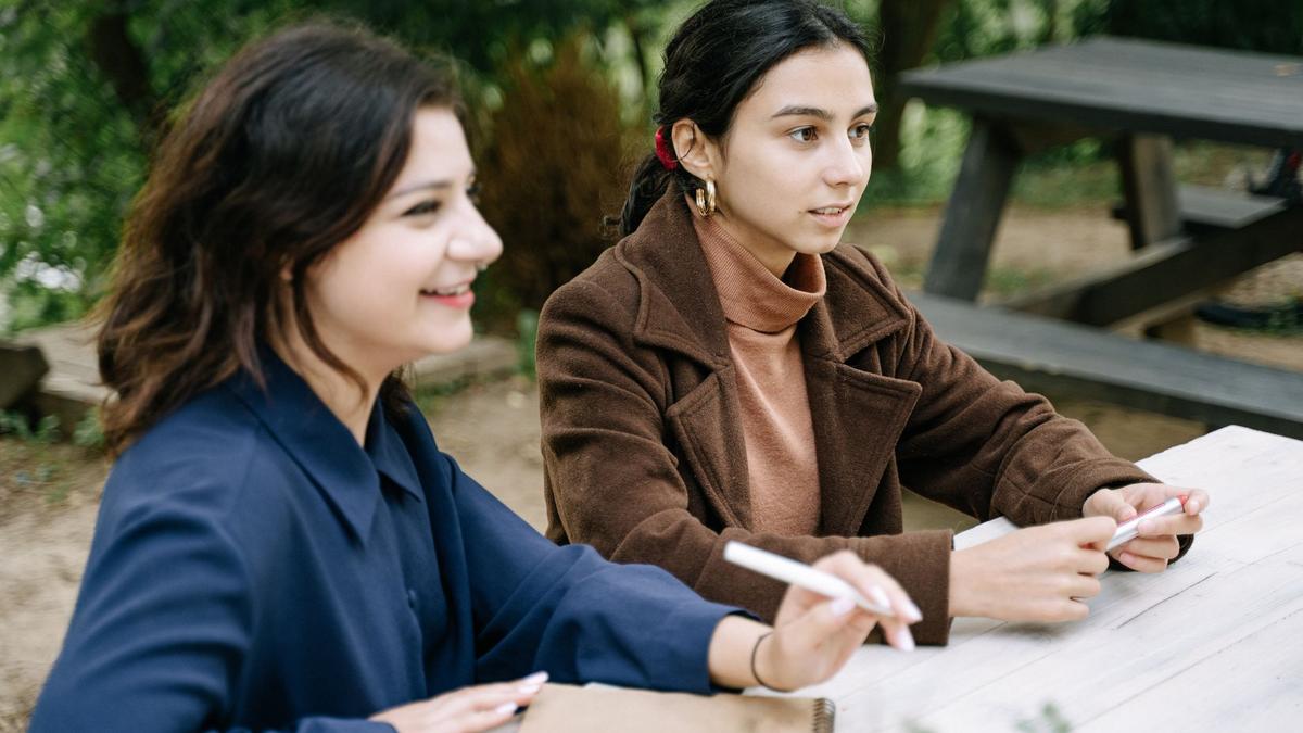 Two young women engaged in a collaborative discussion at an outdoor picnic table.