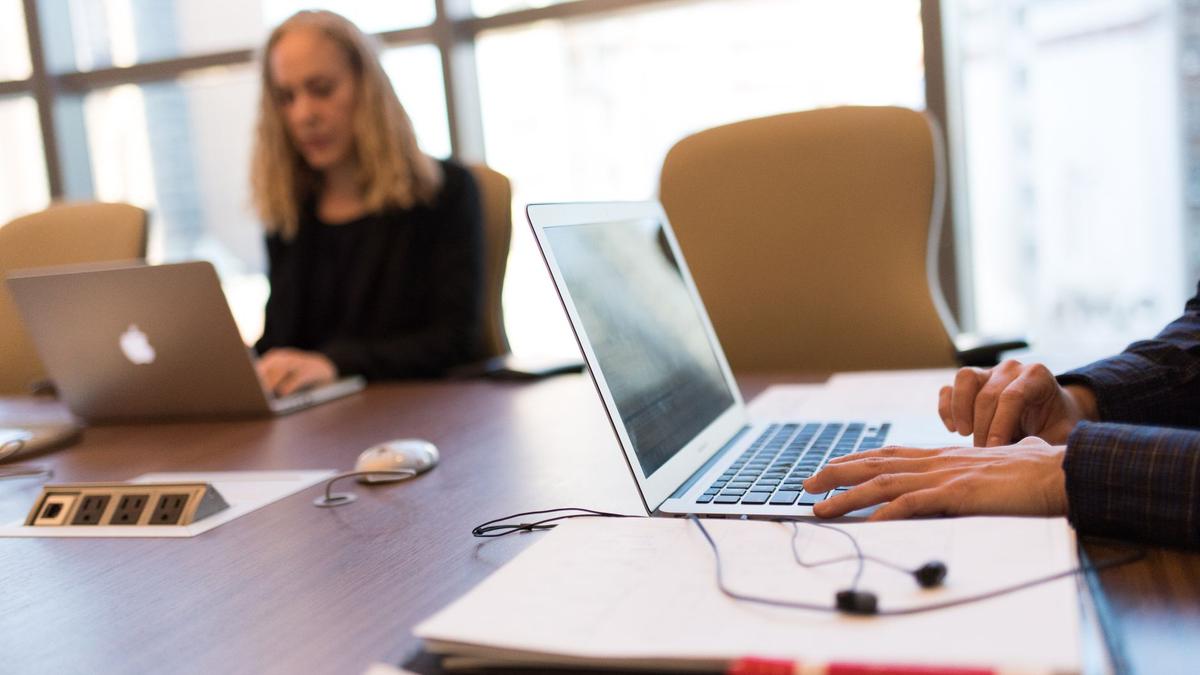 Colleagues collaborating in a bright, modern office setting, focused on laptop work.