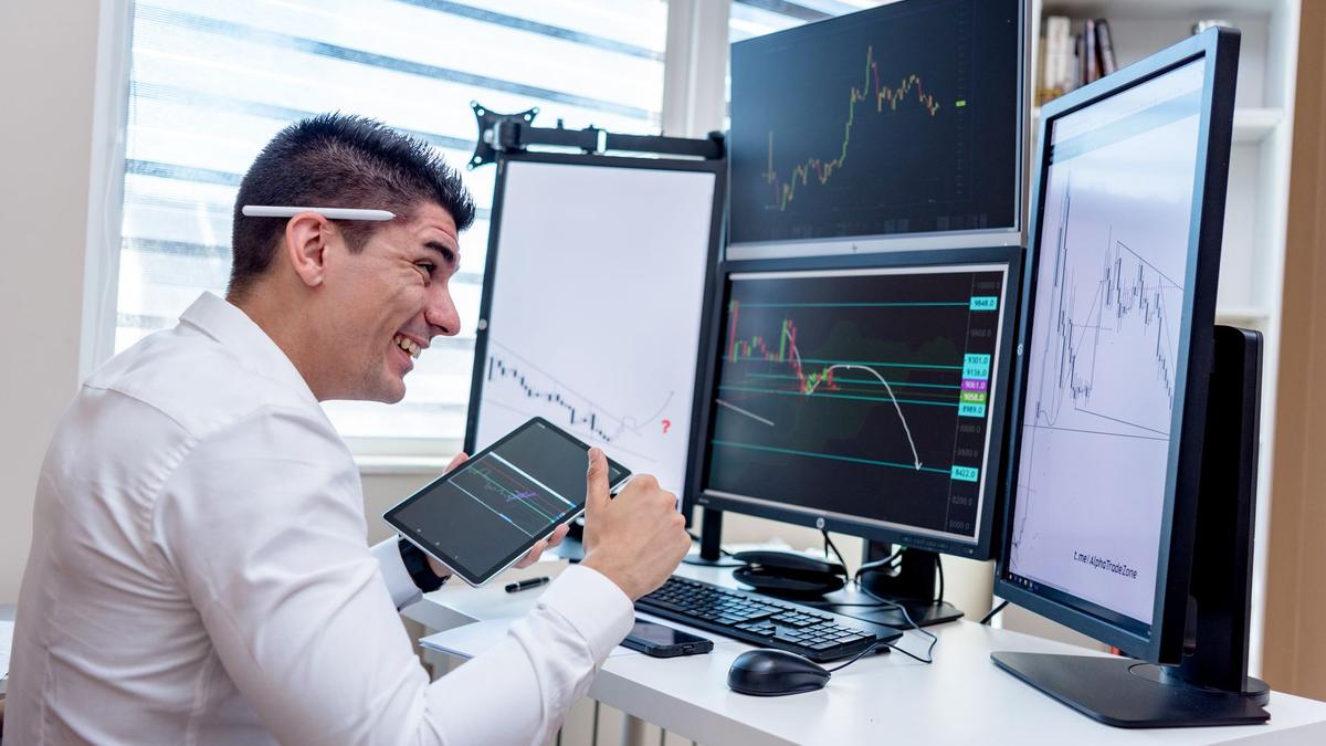A man engaged in financial data analysis on multiple monitors in an office setting.