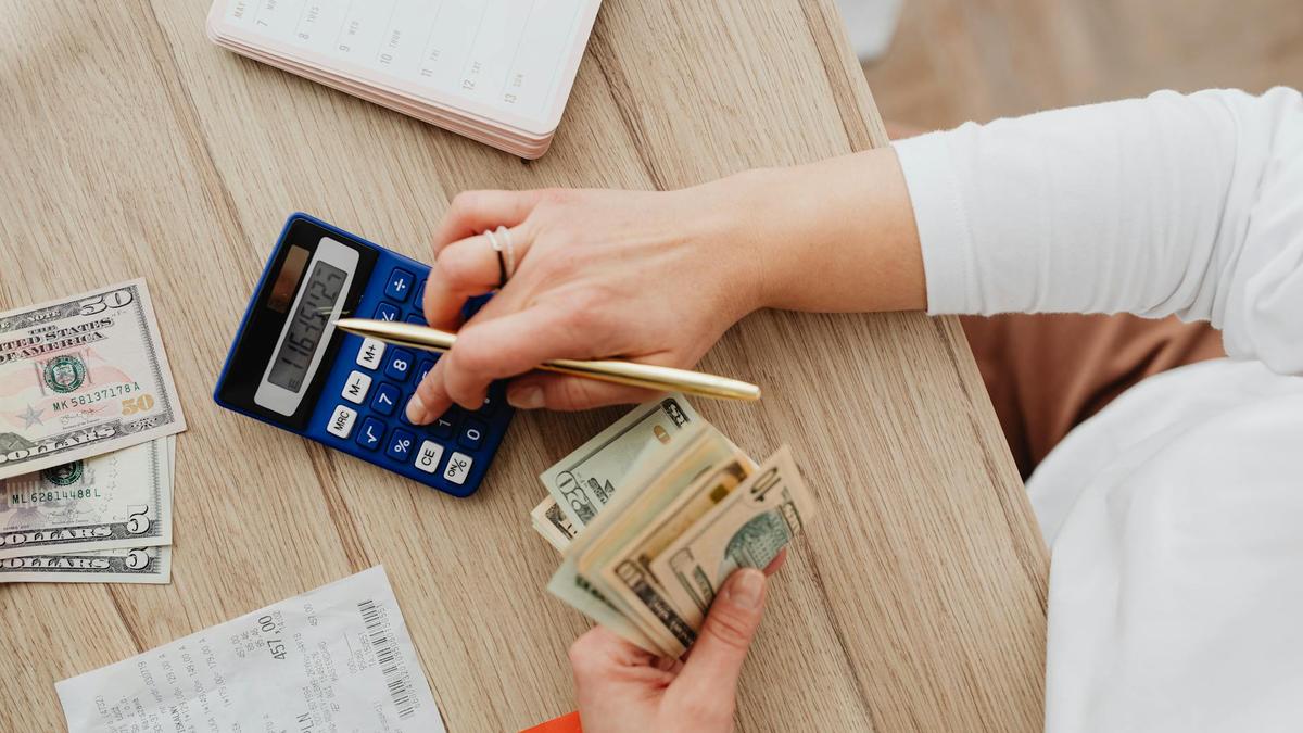 Person using a calculator and counting cash on a wooden table with receipts.