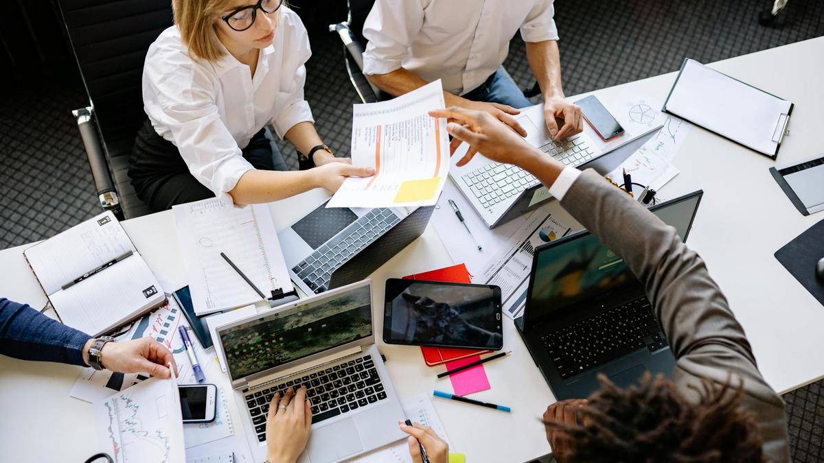 Diverse team collaborating in a modern office with laptops and documents.