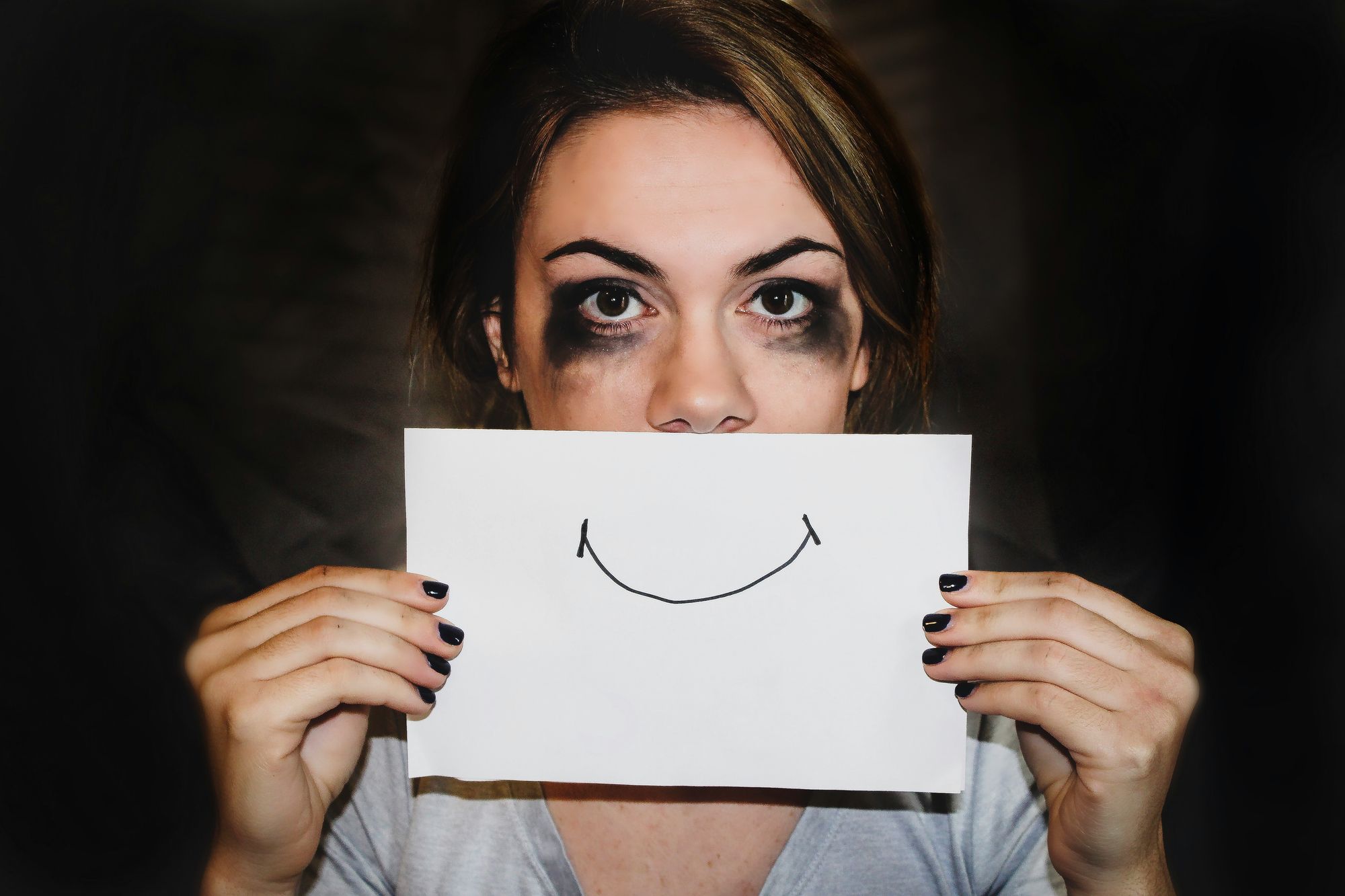 Distressed woman holding up a card with a smile drawn on it to cover her mouth