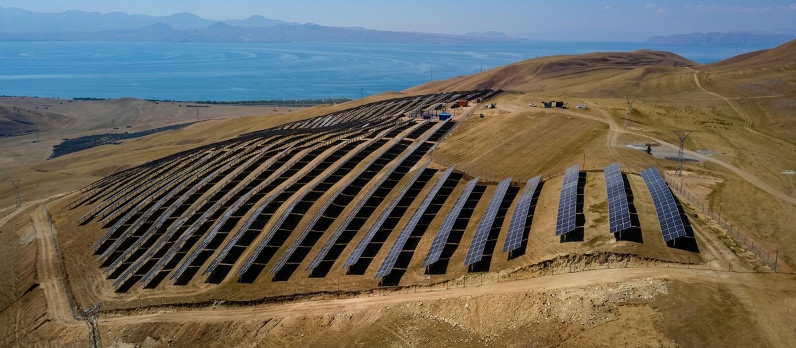 Aerial view of the SOLAR-5 power plant: rows of solar panels curving across a dry hillside above Lake Sevan, with mountains on the far shore.
