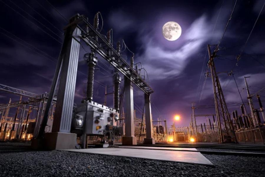 A high-voltage substation gantry and disconnectors photographed at night under a full moon.