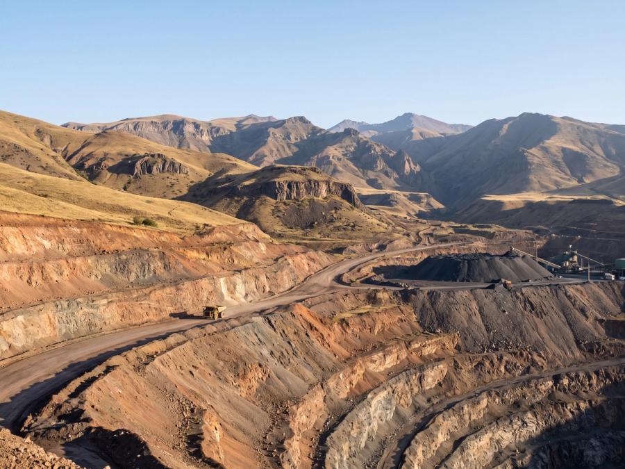 Open-pit copper mine in the Armenian mountains with terraced benches and a haul road.