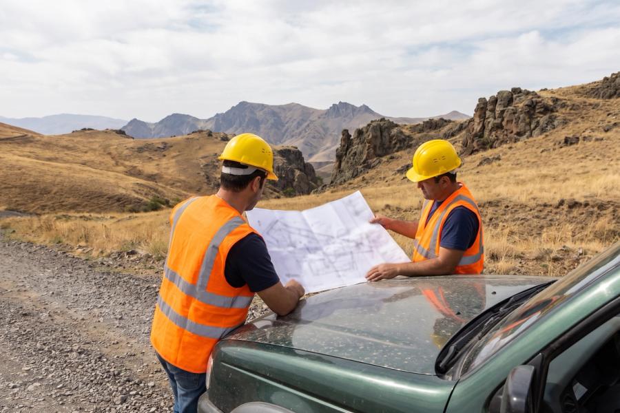 Two engineers in hard hats reviewing a site plan on the hood of a pickup at a mine site.