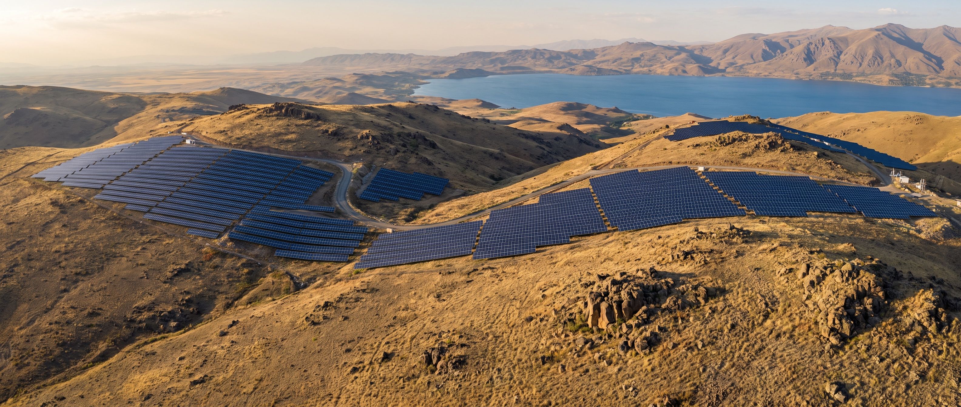 Aerial view of a utility-scale solar power plant on dry hills above a mountain lake in the Armenian highlands.