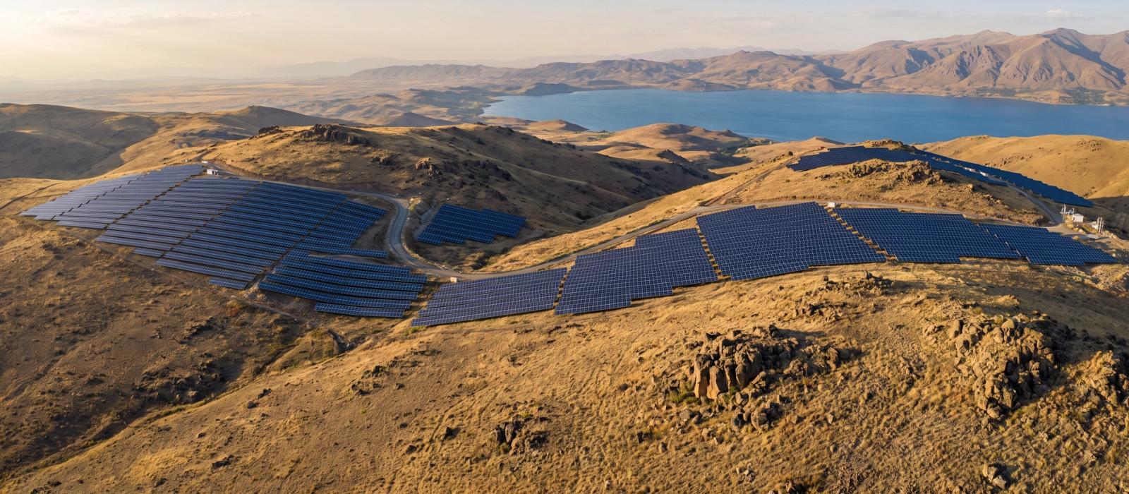 Aerial view of a utility-scale solar power plant on dry hills above a mountain lake in the Armenian highlands.
