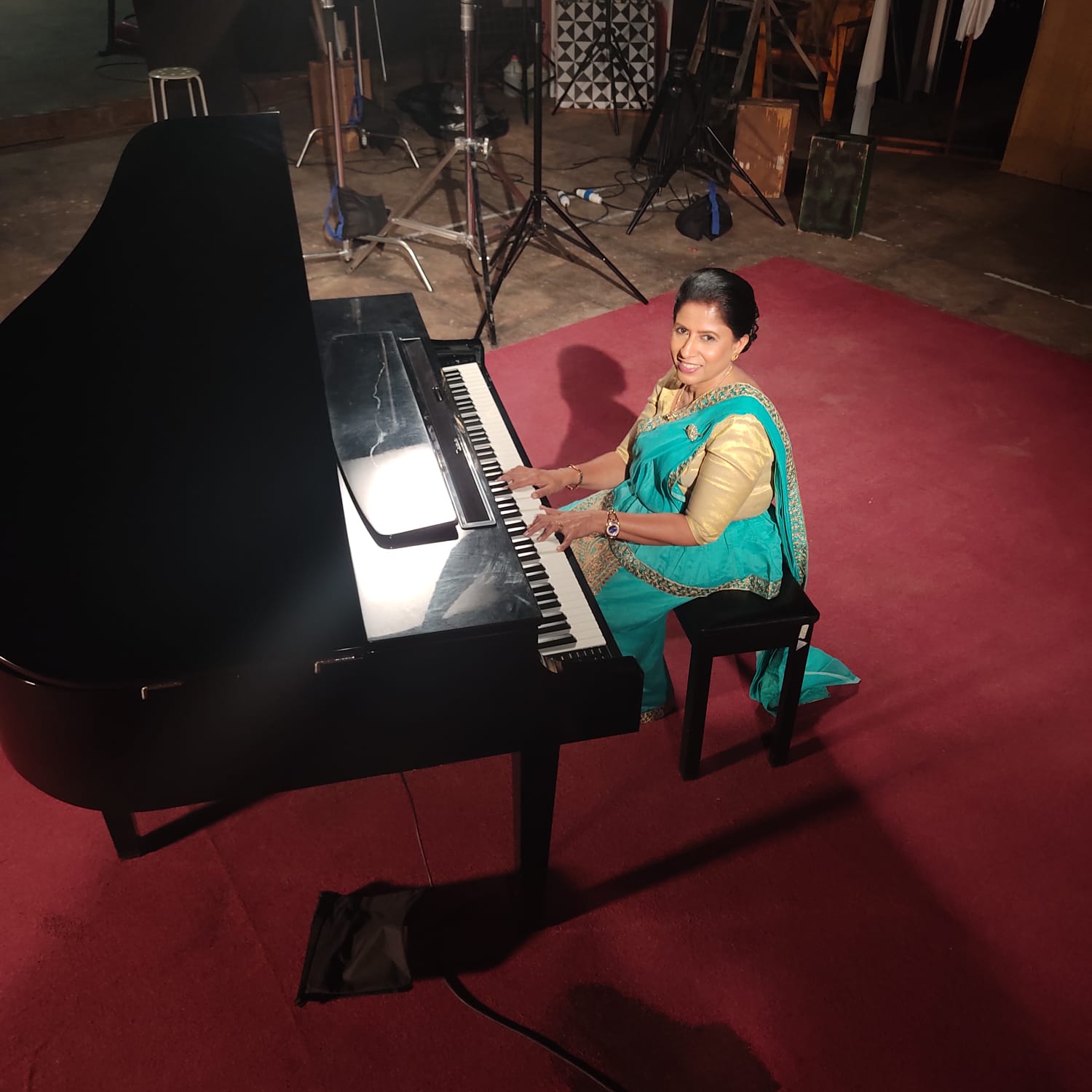 Darshani Chandrasena at a grand piano in a turquoise sari, looking up and smiling
