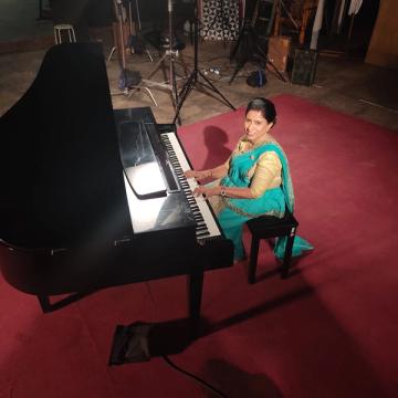 Darshani Chandrasena at the grand piano, red carpet and stage lighting stands around her