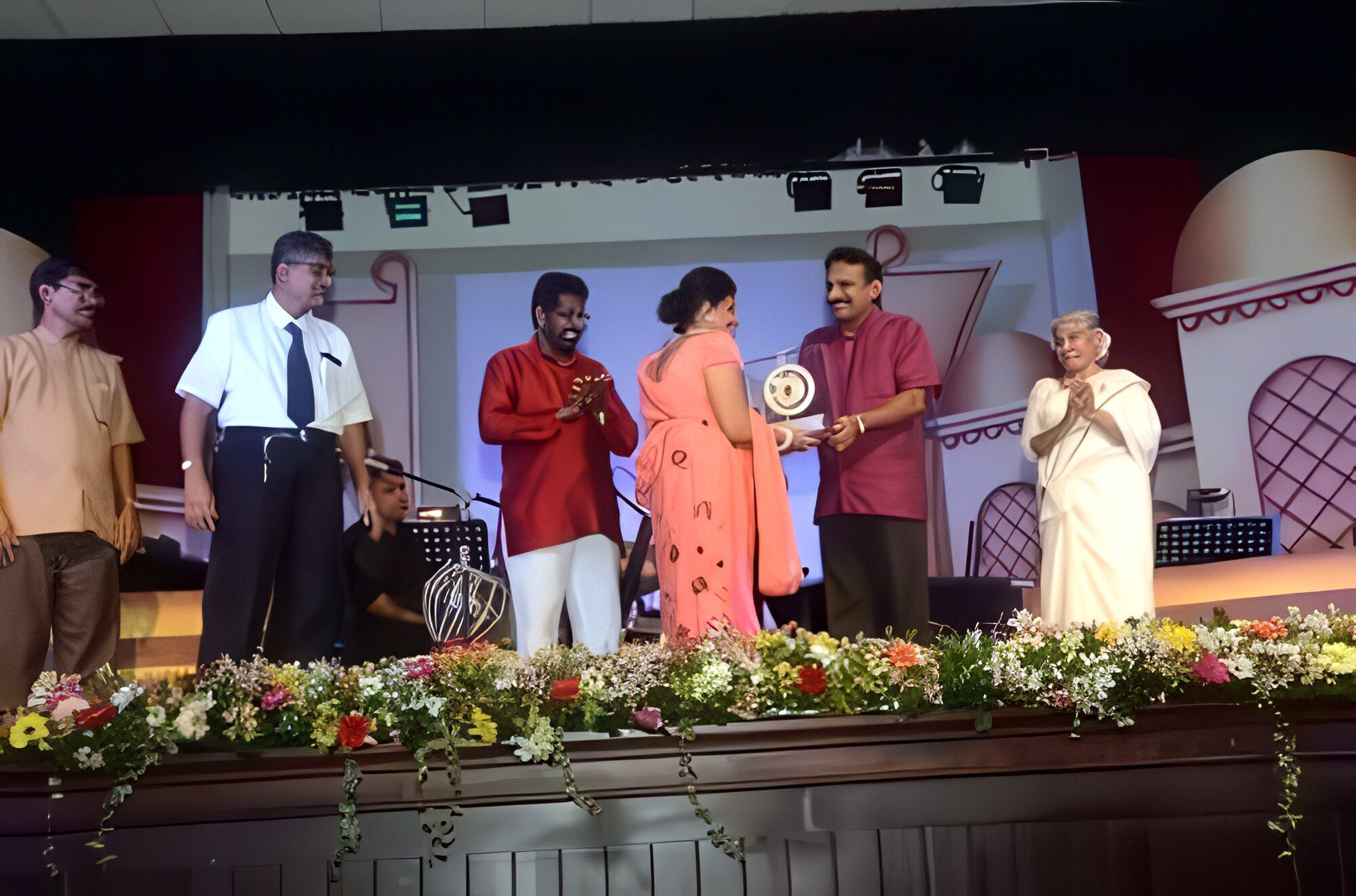 On a flower-lined stage, Darshani Chandrasena accepts a round trophy as an elder in white applauds