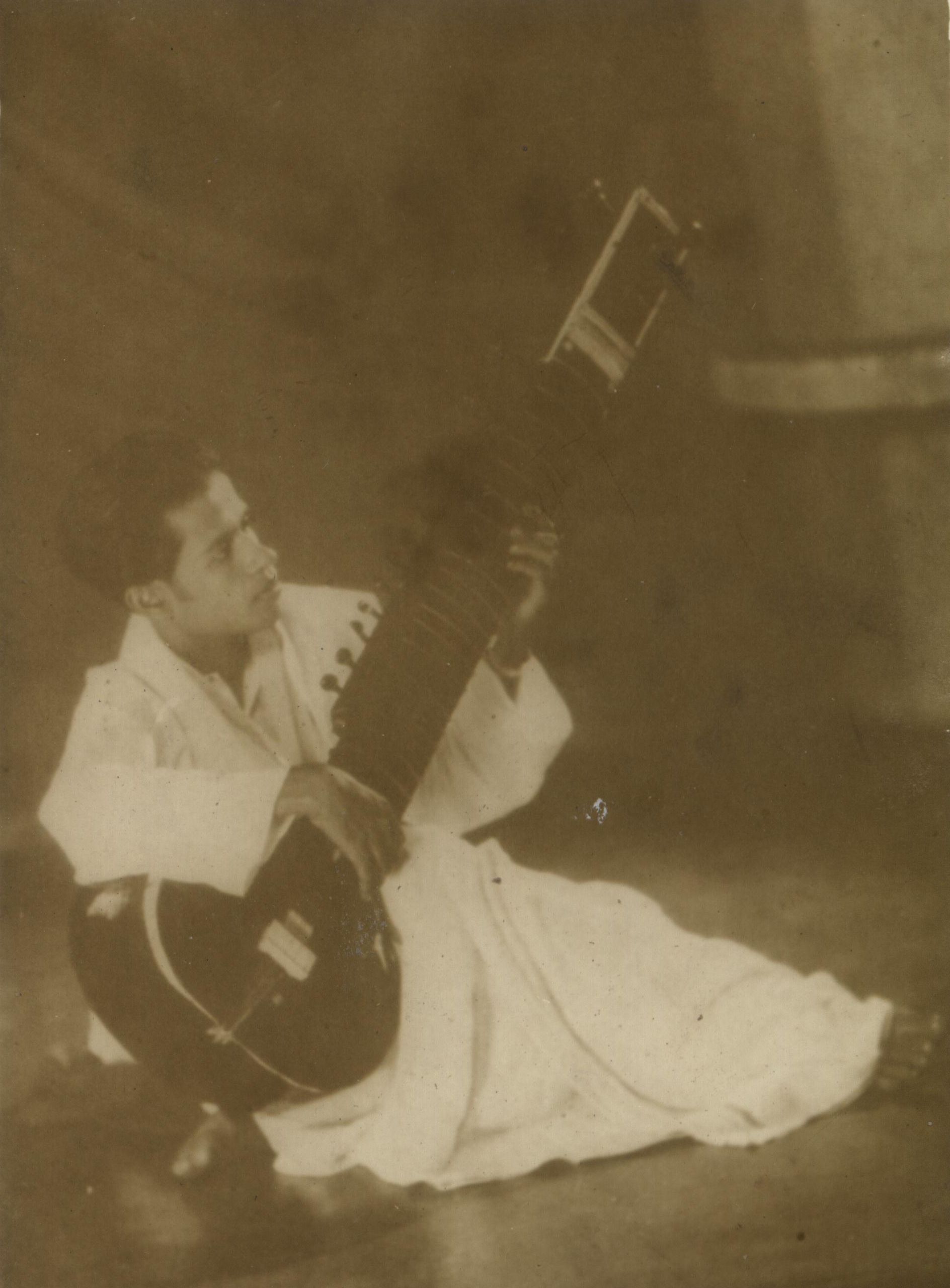 R. A. Chandrasena as a young man, seated cross-legged playing a sitar; aged sepia print