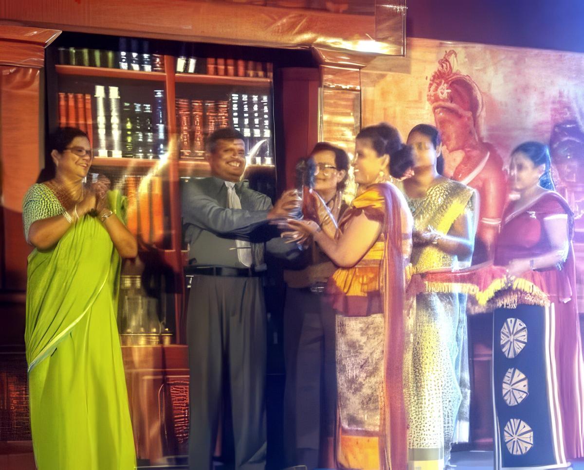 Before a painted stage backdrop, Darshani Chandrasena accepts a crystal trophy