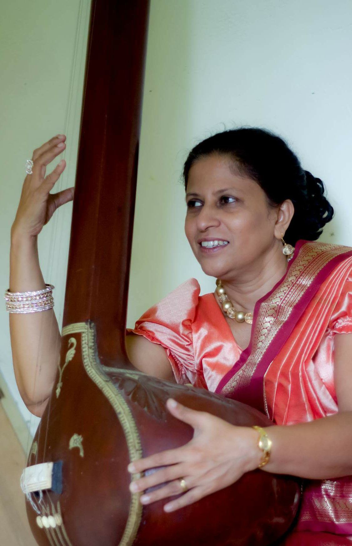 Darshani Chandrasena in a coral sari, smiling as she plays the tanpura