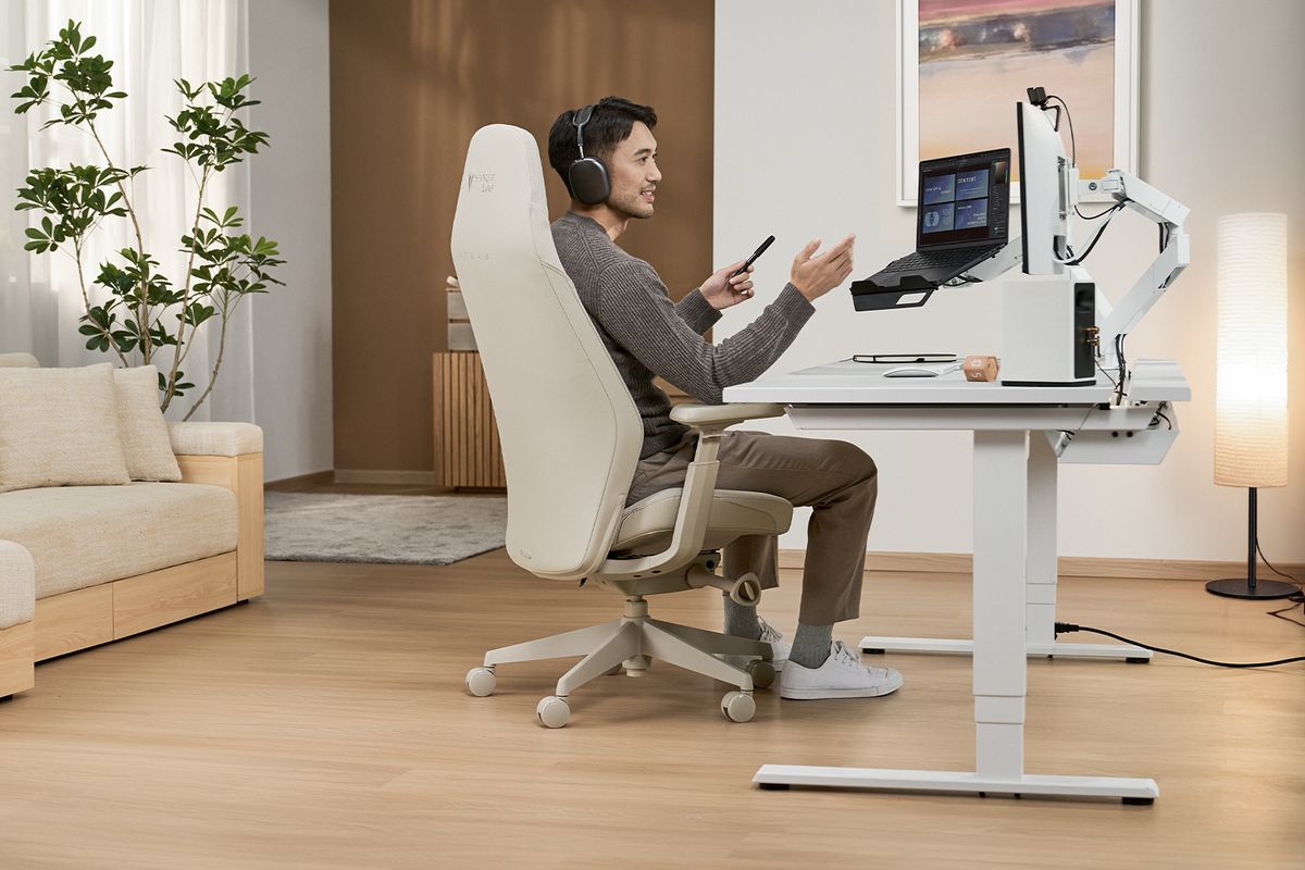 A person seated in a beige Secretlab ATLAS chair at a home office desk.