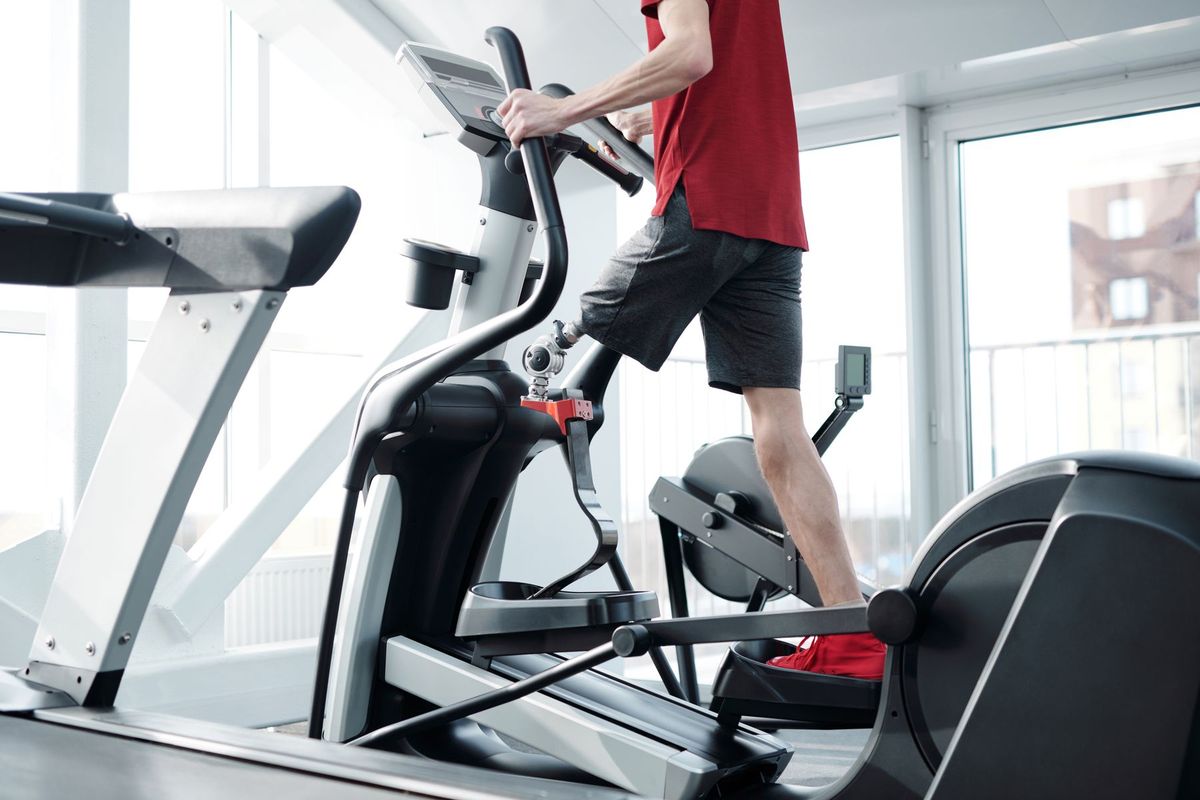 Person with a prosthetic leg using an elliptical trainer in a bright gym.