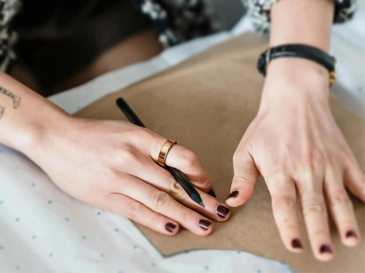 A gold RingConn Gen 2 smart ring worn while writing with a pencil.