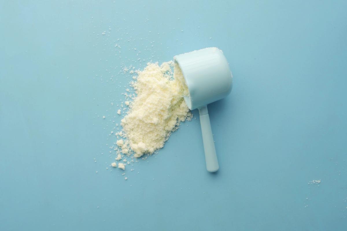White supplement powder spilling from a measuring scoop on a light blue surface