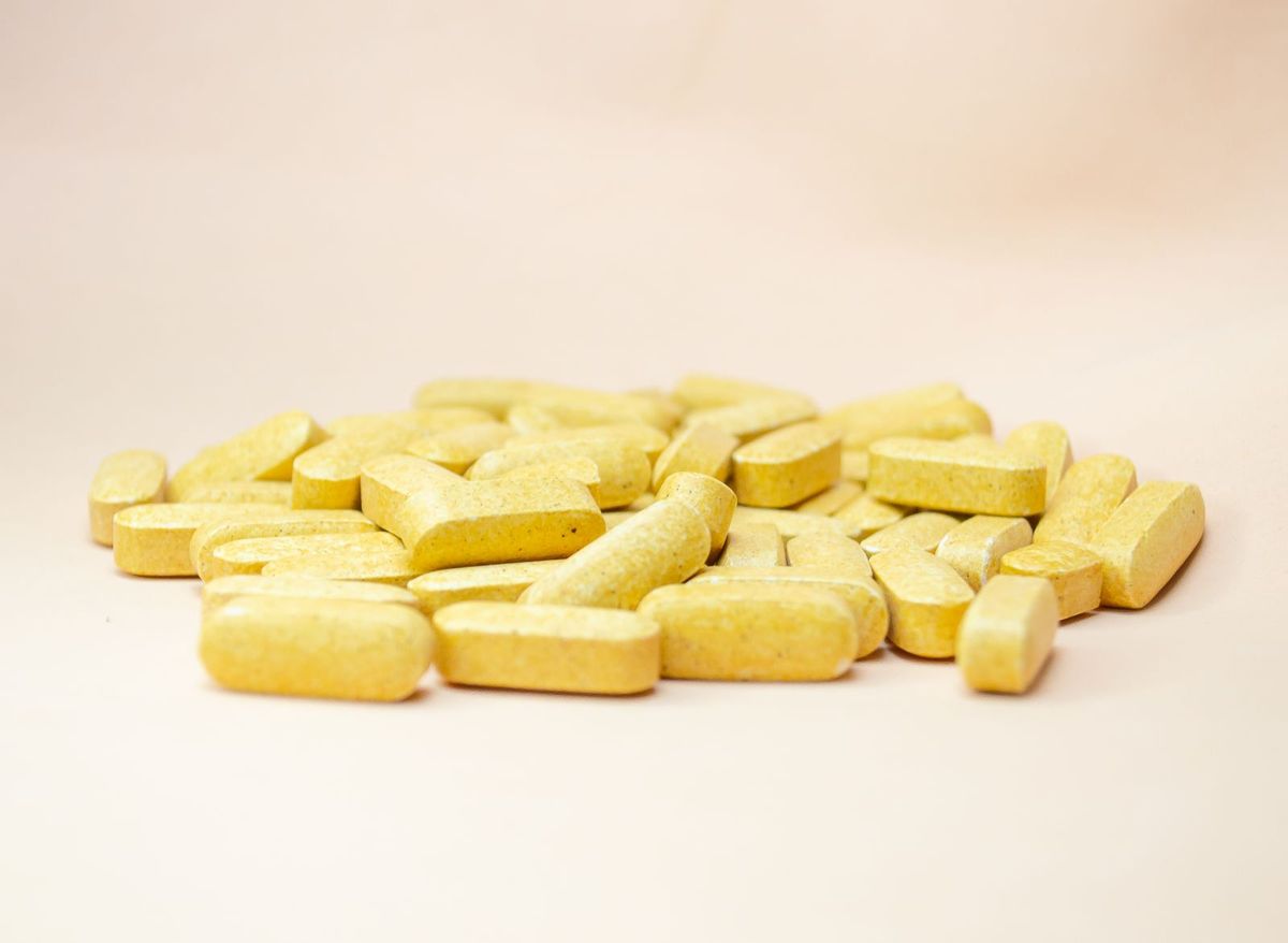 A pile of yellow vitamin tablets on a light beige background.