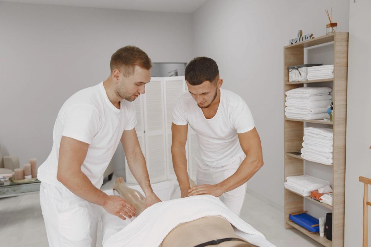 Two massage therapists in white uniforms work on a client in a bright treatment room