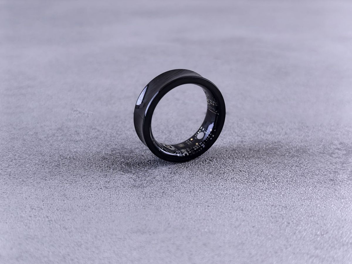 Black smart ring with visible inner sensors standing on a light textured surface.