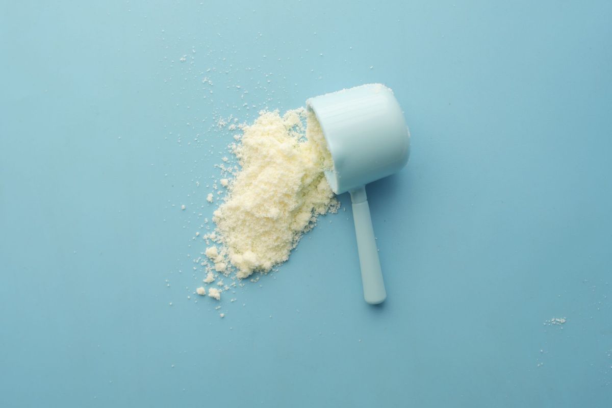 White supplement powder spilling from a measuring scoop on a light blue background.