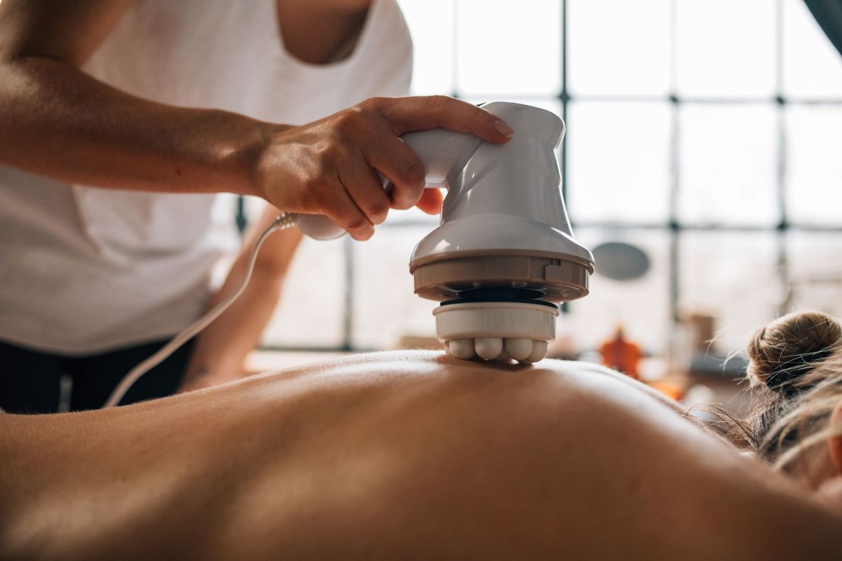 A handheld electric massager being used on a person’s back.